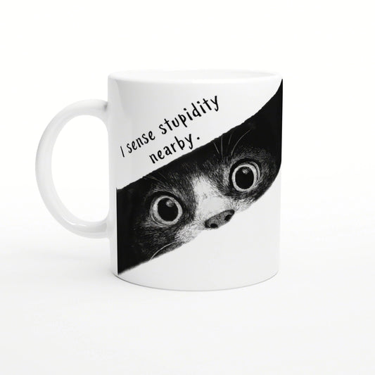 White mug with a black-and-white illustration of a wide-eyed animal peeking from a torn banner that reads I sense stupidity nearby