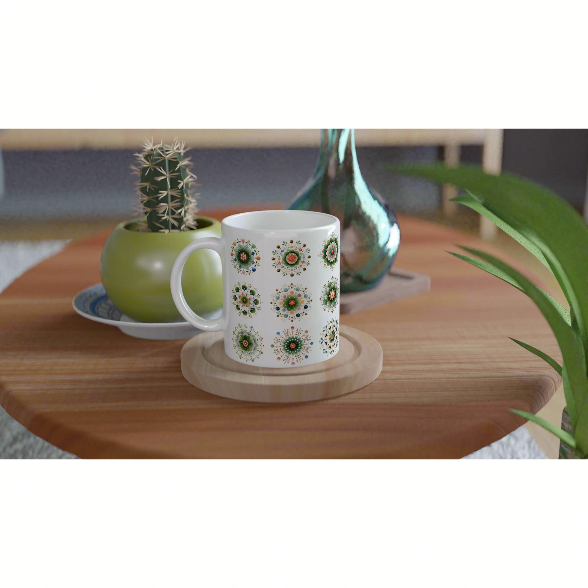 White mug with circular floral patterns on a wooden coaster, on a table with a cactus pot and turquoise vase.